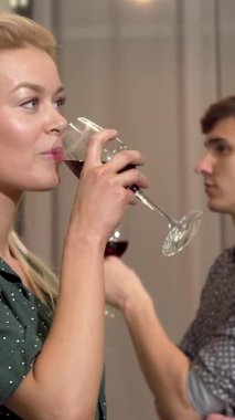 Neşeli bir çift, zengin kırmızı şarap kadehlerini modern bir dairede kaldırarak hassas bir anı paylaşıyor. Güzel kadın, sıcak ve samimi kahkahalarla dolu romantik bir akşamda mutlulukla, sevgiyle ve bağlantıyla ışıldıyor.