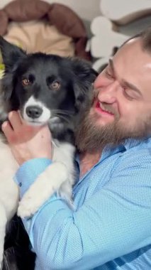 Şık sakallı neşeli bir adam neşeli köpeğini kucaklıyor. Her ikisi de renkli oyuncaklar ve rahat evcil hayvan yataklarıyla dolu canlı bir evcil hayvan dükkanında mutluluk saçıyor. Tapılası köpek, parlak siyah beyaz kürkü ve sallanan kuyruğuyla, sıcaklığı arttırır.