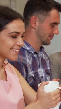 Işıl ışıl bir kız öğrenci, neşeli bir sınıfta arkadaşlarıyla birlikte çalışırken, neşe ve güven dolu bir şekilde başparmağını kaldırıyor. Bu dinamik sahne takım çalışmasının ve coşkunun ruhunu ön plana çıkarıyor. Pembe bluzlu şık bir kadın.