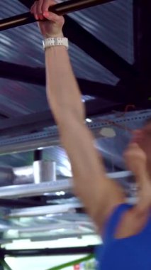 Odaklanmış genç bir kadın barfiks çekerken dikkat çekici bir hassasiyetle etkileyici gücünü ve atletizmini gösteriyor. Beyaz tenli güçlü sporcu barın üzerinde dinamik bir şekilde sallanıyor, zindelik ve kararlılık ruhunu canlı bir şekilde somutlaştırıyor.