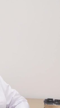 Deniz mavisi aksanıyla bembeyaz bir ceket giymiş dingin, olgun bir kadın doktor, minimalist ofisinde sıcak bir fincan kahvenin keyfini çıkararak gününü yansıtıyor. Bu sakin sahne, kendine bakmanın güzelliğini ve kendine zaman ayırmanın önemini temsil ediyor.