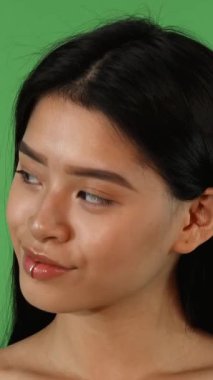 Çekici genç bir Asyalı kadın zarif bir şekilde kenarlara bakar, uzun, ipeksi koyu saçları zarif bir şekilde akarken, yüzünü aydınlatan büyüleyici bir gülümseme ortaya çıkar. Parlak yeşil bir krom anahtar arkaplan ile ayarlandığında, bu an yayılır