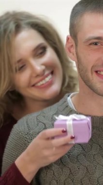 Hoş süveter giyen neşeli bir kadın, her ikisi de Noel Baba şapkasıyla süslenmiş, keyifli erkek arkadaşına eğlenceli bir mor hediye kutusu sunar. Bu yürek ısıtan an aşk ve neşe saçıyor. Kış kutlamalarının özünü mükemmel bir şekilde yakalıyor.