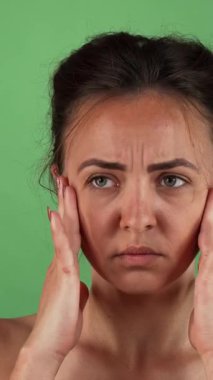 Kaşları çatık ve gergin bir ifadeyle çarpıcı genç bir kadın şakaklarını parlak yeşil renkli bir arka plana nazikçe sürtüyor. Bu çarpıcı görüntü anksiyete ve stresin ağırlığını güçlü bir şekilde yakalıyor ve izleyicileri kendisiyle bağlantı kurmaya çağırıyor.