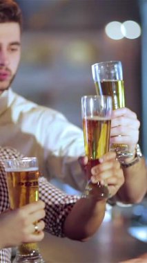 Dört genç adam şık şık ve şık giyinmiş, neşeli bir şekilde altın bira kadehlerini kaldırarak coşkulu bir barın canlı atmosferiyle çevrelenmiş bir şekilde kadeh kaldırıyorlar. Bulaşıcı kahkahaları ve tezahüratları havada yankılanıyor.