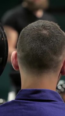 Yetenekli bir berber yakışıklı bir müşteriye şık bir kısa saç kesimini ustalıkla gösterir, o da aynaya özgüvenle bakar. Modern berber dükkânı enerji ile uğulduyor, gösterişli dekorlar ve erkeksi görünüşü yükselten üst düzey tımar araçları var.