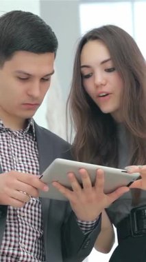 Canlı genç bir çift, takım elbiseli bir adam ve şık kıyafetli bir kadın, heyecan verici bir şekilde iş sonuçlarını parlak bir tablet üzerinde analiz ediyorlar. Animasyon ifadeleri ve yakın işbirliği, başarının heyecan verici atmosferini vurguluyor.