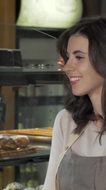 Lezzetli genç bir fırıncı, ağız sulandırıcı hamur işleri ve zanaatkar ekmekleriyle dolu fırınında gururla duruyor. Sıcak gülüşü ve davetkar tavırları müşterileri cezbedici bir atmosfer yaratıyor.