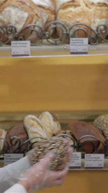 Dalgalı kahverengi saçlı neşeli beyaz bir kadın taze pişmiş bir çavdar ekmeğini hareketli bir fırının kırsal ahşap rafına koyuyor. Sıcak gülümsemesi neşe saçıyor, müşterileri hoş kokuların ve zanaatkârlığın tadına varmaya davet ediyor.