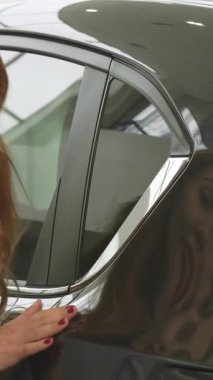 Güzel bir genç kadının büyüleyici yakın çekimi dalgalı kızıl saçlarıyla, galeride parlak bir arabanın parıltılı yüzeyini zevkle okşuyor. Onun ışıl ışıl gülüşü ve ışıl ışıl gözleri yeni bir araç seçmenin heyecanını yansıtıyor.