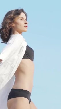 Parlak mavi gökyüzünün altında ışıl ışıl dans eden parlak bir kadın, siyah bikinisi dalgalı beyaz gömleğiyle zarifçe zıt düşüyor. Bu büyüleyici sahne özgürlüğü ve canlılığı simgeliyor. Atletik zarafetini ve sanatsal yeteneğini sergiliyor.