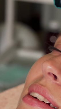 Huzurlu genç bir kadın ultrasonik bir yüz tedavisinden zevk alırken rahatlamanın tadını çıkarıyor. Gözleri tamamen mutlulukla kapanıyor. Uzman güzellik uzmanı gelişmiş ultrasonik aletleri ustalıkla kullanıyor. Cildini temizliyor ve gençleştiriyor.