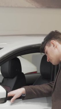 Olgun bir adam, şatafatlı bir galeride lüks bir arabanın içini merakla inceliyor. Bu büyüleyici sahne araba alışverişinin heyecanını, modern tasarımı ve potansiyel sahipliğin heyecanını somutlaştırıyor.