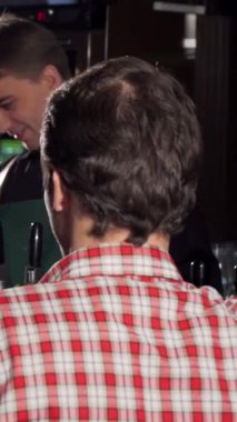 Çekici genç bir adam canlı bir bar ortamında arkadaşıyla neşeyle kadeh tokuştururken kameraya ışıldıyor. Sıcak ışıklandırma ve zengin ahşap dokular dostluğu ve güzel zamanları bira içerek kutlayan davetkar bir atmosfer yaratıyor.