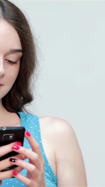 Dalgalı kahverengi saçlı neşeli bir genç kız akıllı telefonuyla meşgul olurken, şakacı bir şekilde başparmağını kaldırıyor. Canlı mavi bir atlet gibi giyinmiş, neşeli tavırları pozitiflik saçıyor, bağlantıyı davet ediyor ve heyecanını gösteriyor.