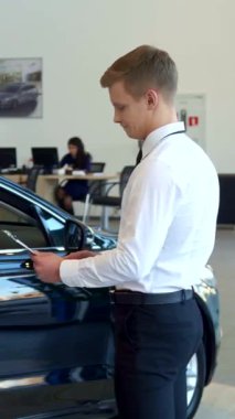 Gösterişli, modern bir bayilikte, genç bir çift büyüleyici siyah bir aracın yanında profesyonel bir satıcıyla yapılan sözleşmeyi heyecanla inceliyor. Potansiyel alımları hakkında dinamik bir tartışmaya girdiklerinde hava beklenti ile doludur.