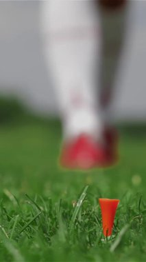 Kızıl saçlı zarif bir bayan golfçü, eldivenli elini nazik bir şekilde turuncu renkli bir tişörtün üzerine yerleştirmeye hazırlanıyor. Bu yakın çekim onun yoğun odaklanma ve şık davranışlarını yakalıyor yemyeşil bir zemin üzerinde