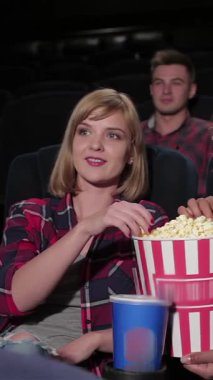 Pofuduk kırmızı tiyatro sandalyelerinde oturan canlı bir grup genç arkadaş, rahat bir multipleks 'te heyecanlı bir film izlemek için can atıyorlar. Patlamış mısır kovaları taşar ve kahkahalar yankılanır. Neşeli ifadeleri mükemmel bir film gecesinin özünü yakalar.