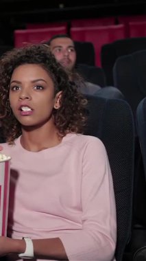 Canlı bir grup genç arkadaş, kahkaha ve patlamış mısırlarını paylaşırken gözleri ekrana yapışık, rahat bir multipleks tiyatroya dalmış. Atmosfer heyecanla uğulduyor, arkadaşlığın özünü ve sinemanın neşesini yakalıyor.