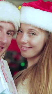 Mutlu bir çift, rahat tatil kazakları ve kabarık Noel Baba şapkaları giyerek, güzel süslenmiş bir odada birbirlerine hediye verirken mutluluk saçıyorlar. Yanıp sönen ışıklar ve göz kamaştıran bir Noel ağacı ile çevrelenmiş sıcak gülümsemeleri.