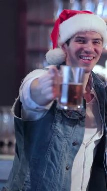 Şenlikli Noel Baba şapkalı arkadaşlar bardaklarını sevinçle kaldırırken coşkulu bir kutlama başlıyor. İçtenlik ve dostluk saçıyorlar. Barmen arka planda ışıldıyor, bayram neşesinin ve beraberliğin heyecanını yakalıyor.