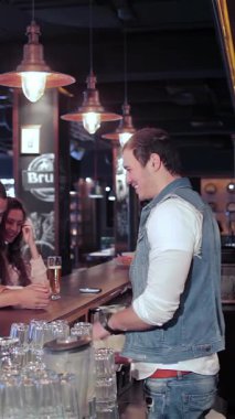 Enerjiyle dolu canlı bir barda, iki neşeli kız ve bir adam canlandırıcı bir şekilde içkilerini sipariş eder, kahkahaları canlı atmosferde yankılanır. Bar ışıklarının sıcacık parlaklığı ve bardakların tıkırtısı şenlikli bir zemin oluşturur.