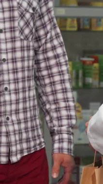 Parlak ve düzenli bir eczanede, beyaz önlüklü profesyonel bir eczacı şık ekose gömlekli memnun bir erkek müşteriyle el sıkışıyor, güveni ve sağlık hizmetlerindeki istisnai hizmeti sembolize ediyor. Canlı raflar dolu.