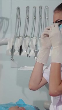 Modern bir diş muayenehanesinde parlak ışıkla yıkanan şık gözlüklü ve beyaz önlüklü neşeli bir dişçi hastalarının ağzını dikkatlice inceliyor. Çekici sarışın hasta, dişçi koltuğunda rahat, sıcak ve davetkar