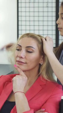 Şık bir güzellik salonunda, ışıl ışıl bir kadın düşünceli bir gülümsemeyle poz verir ve sevimli kızı uzun, dalgalı saçlarını şekillendirir. Bu büyüleyici an, aile bağlarının mutluluğunu güzel bir şekilde yansıtıyor.