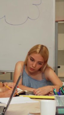 Uzun sarı saçlı, kendini işine adamış genç bir kız öğrenci notlarını dikkatle incelerken çevresi parlak ve modern bir çalışma alanıyla çevrili. Konsantrasyonu ve öğrenmeye olan bağlılığı sayesinde ekip çalışmasında ilham verici bir atmosfer yaratıyor.