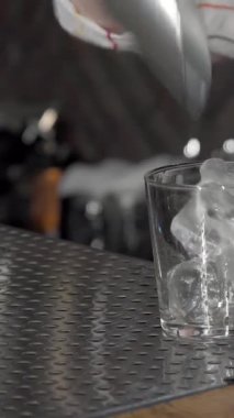 Yetenekli bir bayan barmen zarif bir şekilde pırıl pırıl buzları üzerine parlak bir bardakla zengin viski dökerek, sanatını parlak barın arkasında sergiliyor. Işıldayan tezgahı ve şık kokteyl sallayıcısı ile canlı bir ortam, davetkar bir davet yaratır.