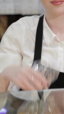 Pişmiş malların hoş aromasıyla dolu sıcacık bir fırında gevrek beyaz gömlek ve önlüklü neşeli genç bir kadın bir dizi yeni paketlenmiş rulo sunar. Çekici gülüşü ve yuvarlakların altın kabukları bir atmosfer yaratıyor.