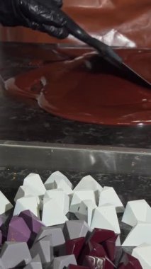 Kendini adamış, siyah eldivenlere bürünmüş, titiz bir şekilde zengin, parlak bir mermer yüzey üzerinde parlak bir çikolata, canlı, geometrik kalıplarla çevrili. Bu büyüleyici sahne küçük bir işletmenin sanatını ve tutkusunu yansıtıyor.