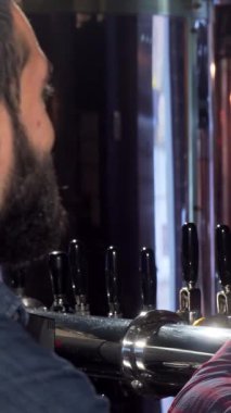 Ekose gömlekli ve önlüklü neşeli bir barmen neşeyle bir müşteriyle kadeh tokuşturur, kahkaha ve dostluk saçar. Parıldayan musluklar ve köpüklü bira ile vurgulanan barlar, coşkulu bir kutlama ve bağ sahnesi hazırlar.