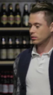 Canlı bir içki dükkanında, şık bir genç adam renkli bira şişelerini dikkatle inceliyor, sezgisel zevkini sergiliyor. Cazip etiketlerle dolu canlı raflar heyecan ve modern bir atmosfer yaratıyor.