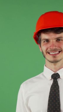 Parlak turuncu bir şapkayla süslenmiş şık bir erkek mühendis, kameraya neşeli bir şekilde göz kırpıyor, canlı yeşil bir kromakey arka planına karşı bir cazibe yayıyor. Bulaşıcı gülümsemesi ve kendine güveni inşaat endüstrisine olan tutkuyu yansıtıyor.