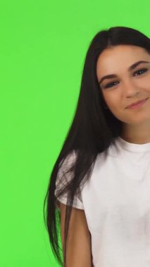 Neşeli, genç, esmer bir kadın mutluluk saçıyor, canlı yeşil bir arka plana neşe içinde barış işareti yapıyor. Büyüleyici gülüşü ve enerjik enerjisi pozitifliği ve sıcaklığı, davetkar bağı ve dostluğu