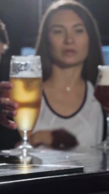 Ön planda çıtır çıtır, altın bir bira bardağı parıldarken, genç bir çift, bir erkek ve bir kadın canlı bir barda kadehlerini neşeyle tokuşturuyorlar. Bu canlı sahne, dostluk ruhunu somutlaştıran sıcaklık ve bağlılık saçıyor.