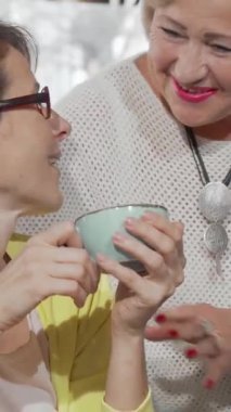 Sıcak bir kahve dükkanında, neşeli yaşlı bir kadın orta yaşlı kızıyla sıcak bir kucaklaşmayı paylaşıyor, gülümsemeleri sevgi ve neşe saçıyor. Bu yürek ısıtan birleşme aile bağının özünü yansıtıyor, kahkaha ve şefkat