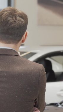 Süslü kahverengi takım elbiseli neşeli, olgun bir adam şık bir bayilikte, göz kamaştırıcı modern araçların arasında rüya arabasını tasarlıyor. İfadesi heyecan ve beklenti yayıyor. Seçme heyecanını somutlaştırıyor.