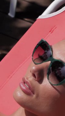 Parlak kızıl saçlı, göz kamaştırıcı genç bir kadın altın güneş altında lüks bir hayat sürüyor. Gözleri şık güneş gözlüklerinin arkasında mutlulukla kapanıyor. Şık pembe bir mayo giymiş, mercan güverte sandalyesinde zarifçe uzanmış, yazın özünü özetliyor.