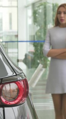 Şık elbiseli şık bir kadın modern bir araba galerisinde düşünceli bir şekilde duruyor. Gözleri parlak sergi odası ışıklarının altında parıldayan parlak bir otomobilde sabitlenmiş. Bu büyüleyici sahne zarafet ve tüketiciliği harmanlıyor ve izleyicileri kendisine davet ediyor.