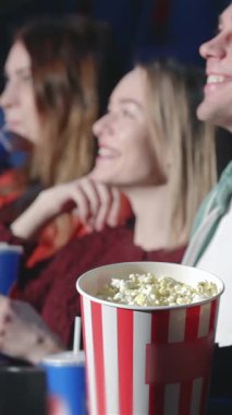 Büyüleyici bir sahnede, sinematik maceraya atlarken yüzleri neşeyle aydınlanmış yedi arkadaş sergileniyor. Patlamış mısırın taşması ve renkli içeceklerle, bu canlı grup mutluluk saçıyor, arkadaşlığın özünü somutlaştırıyor.