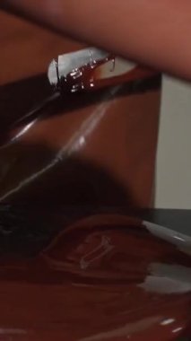 Canlı bir mutfakta, parlak bir önlük ve eldiven giymiş kendini adamış bir çikolatacı, parlak bir tezgahın üzerinde ustalıkla, pürüzsüz, lezzetli bir çikolata yiyor. Bu dinamik sahne, zarif yaratılış arkasındaki titiz sanat ve tutkuyu sergiliyor.