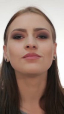 Çekici genç bir kadın kameraya bir öpücük yolluyor büyüleyici gülüşü neşe ve güven saçıyor. El değmemiş beyaz bir arkaplan, çarpıcı özellikleri ve anlamlı gözleri davetkar ve neşeli bir atmosfer yaratıyor.