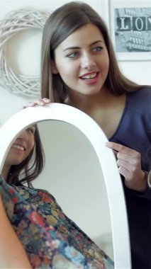 İki modaya uygun kız arkadaş, şık bir aynanın önünde şık bir elbiseyi heyecanlı bir şekilde ölçerken, yüzleri neşe ve heyecanla parlarken aynı anı paylaşıyorlar. Bu canlı sahne, arkadaşlığın özünü ve keşfin heyecanını yansıtıyor.