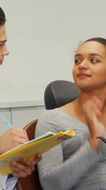 Dost canlısı bir erkek dişçi, güzel Afrikalı kadın hastasıyla sıcak bir konuşma yaparken tıbbi formları dikkatlice doldurur. Bu davet sahnesi profesyonellik ve özen gösteriyor, iletişimin önemini vurguluyor.