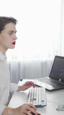 Gıcır gıcır beyaz bir gömlek giyen yorgun genç bir kadın, dizüstü bilgisayarındaki işlerle uğraşırken gözle görülür bir şekilde şaşkına dönmüş bir şekilde modern ofis masasında oturuyor. Perdelerin arasından süzülen yumuşak, parlak ışık onun stresli ifadesini vurguluyor.