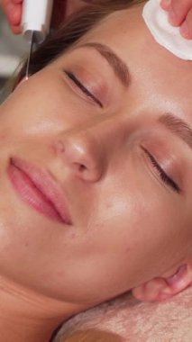 Radyasyon saçan bir kadın, ultrasonik yüz tedavisiyle eğlenirken kameraya ışıl ışıl gülümser. Kusursuz cildi, yumuşak klinik ışıkları altında parlar. Becerikli bir güzellik uzmanı tarafından tamamlanan sakin spa ortamı, tedaviyi nazikçe uyguluyor.