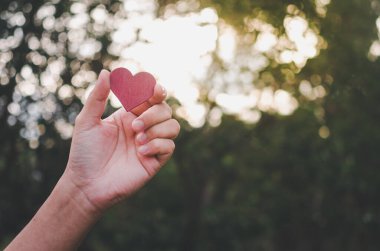 human hand holds red heart shaped wood piece